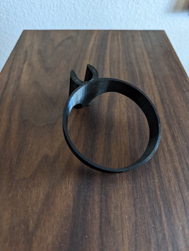 May include: A black plastic cup holder with a simple design. The holder is designed to fit around a standard-sized cup.