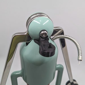 Pode incluir: Uma cafeteira azul-esverdeada com base prateada e uma al&ccedil;a de pl&aacute;stico preto. A cafeteira tem um tubo prateado que se estende do topo.