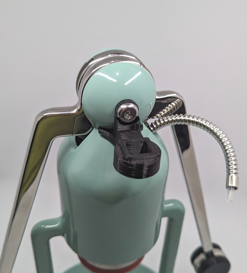 Pode incluir: Uma cafeteira azul-esverdeada com base prateada e uma al&ccedil;a de pl&aacute;stico preto. A cafeteira tem um tubo prateado que se estende do topo.