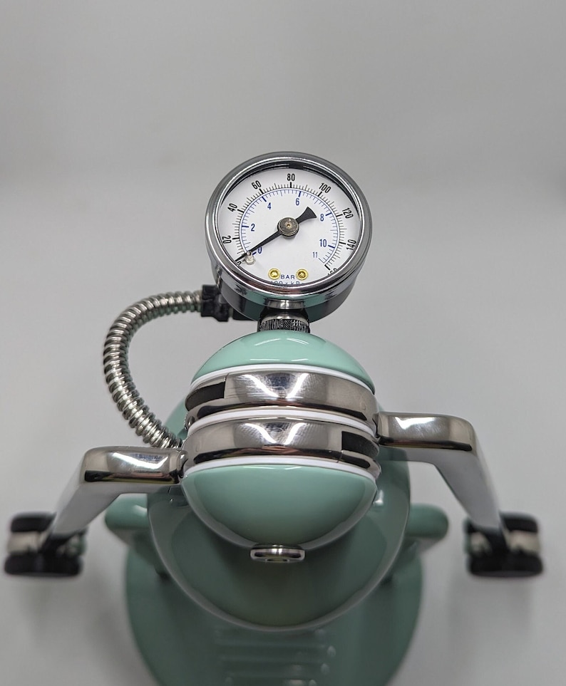 Pode incluir: Close-up de uma m&aacute;quina de caf&eacute; expresso verde com um man&ocirc;metro cromado que l&ecirc; at&eacute; 12 bar. O man&ocirc;metro est&aacute; conectado a um tubo cromado que leva &agrave; m&aacute;quina.