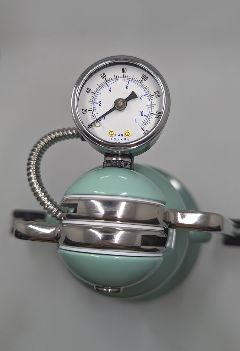 Pode incluir: Um close-up de uma m&aacute;quina de caf&eacute; expresso prateada e verde com um man&ocirc;metro que l&ecirc; at&eacute; 160. O man&ocirc;metro l&ecirc; "BAR 100 x kPa".