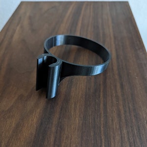 May include: A black plastic ring with a hook on one side. The ring is designed to hold a cup or mug.
