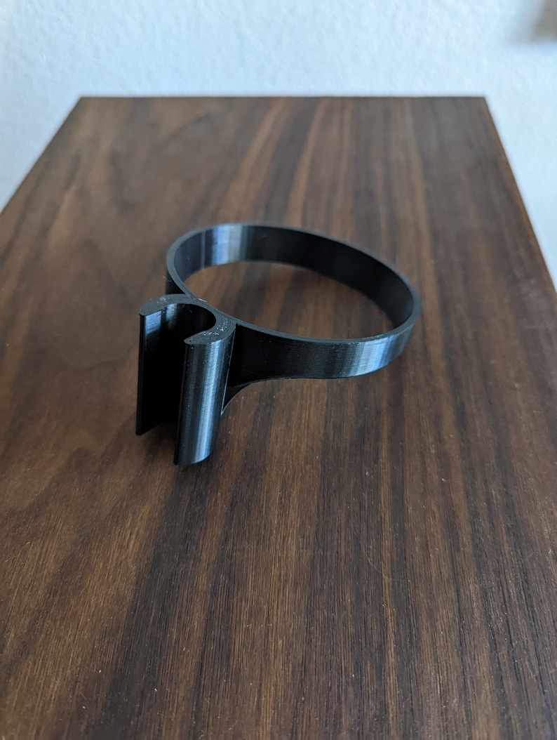 May include: A black plastic ring with a hook on one side. The ring is designed to hold a cup or mug.