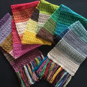 May include: A multi-colored crocheted scarf with a fringe. The scarf is made of different colored yarn, including purple, pink, red, orange, yellow, green, blue, and gray. The fringe is made of a variety of colors, including pink, blue, green, yellow, and red.