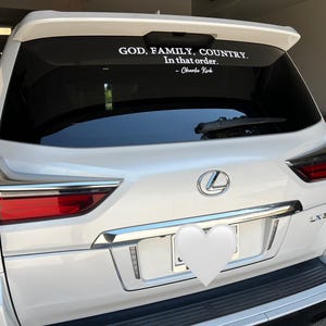 May include: White Lexus SUV with a rear window decal. The decal reads "GOD, FAMILY, COUNTRY. In that order." and is attributed to Charlie Kirk. The vehicle has chrome accents and red taillights.
