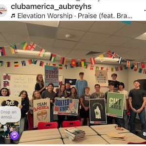 May include: A group of students holding signs with various messages, including "FREE," "TEAM AMERICA," and "CUT TAXES." The room is decorated with flags from different countries and the American flag. The text "DUMP YOUR SOCIALIST BOYFRIEND" is visible.