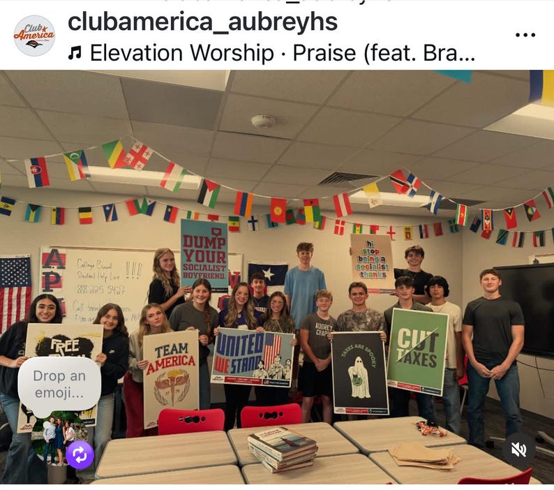 May include: A group of students holding signs with various messages, including "FREE," "TEAM AMERICA," and "CUT TAXES." The room is decorated with flags from different countries and the American flag. The text "DUMP YOUR SOCIALIST BOYFRIEND" is visible.