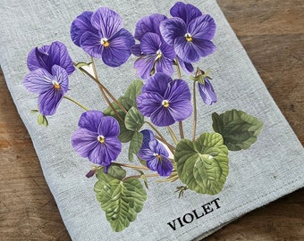 Op de afbeelding: Een grijze linnen theedoek met een paars viooltjesbloemendesign en het woord "VIOLET" in zwart onderaan.