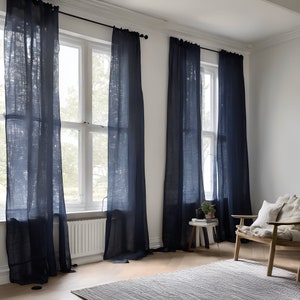 K&ouml;nnte beinhalten: Drei Fenster mit dunkelblauen Leinenvorh&auml;ngen in einem Raum mit wei&szlig;en W&auml;nden und einem Holzstuhl mit einem wei&szlig;en Kissen.