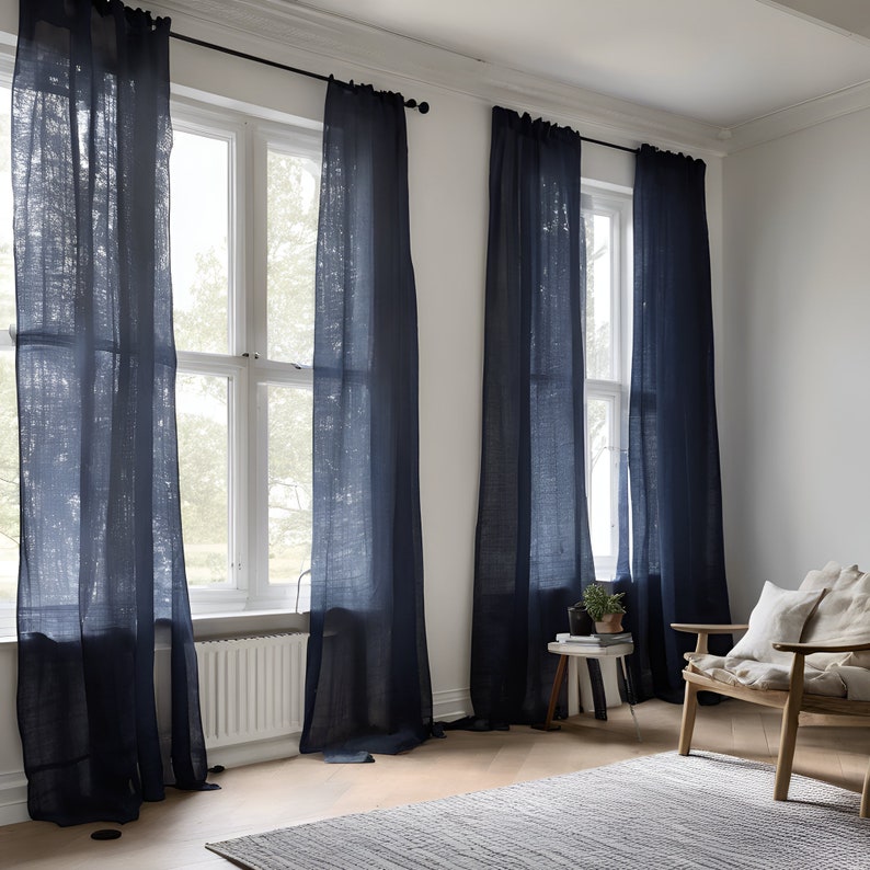 K&ouml;nnte beinhalten: Drei Fenster mit dunkelblauen Leinenvorh&auml;ngen in einem Raum mit wei&szlig;en W&auml;nden und einem Holzstuhl mit einem wei&szlig;en Kissen.