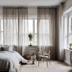 K&ouml;nnte beinhalten: Ein Schlafzimmer mit einem Bett, einem Stuhl und durchsichtigen Vorh&auml;ngen. Das Bett hat eine wei&szlig;e Bettdecke und graue Kissen. Der Stuhl ist aus Holz und hat ein hellgraues Kissen. Die Vorh&auml;nge sind aus hellbraunem Stoff und h&auml;ngen an einer wei&szlig;en Stange.