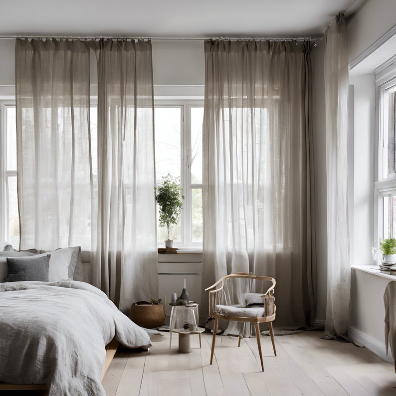 K&ouml;nnte beinhalten: Ein Schlafzimmer mit einem Bett, einem Stuhl und durchsichtigen Vorh&auml;ngen. Das Bett hat eine wei&szlig;e Bettdecke und graue Kissen. Der Stuhl ist aus Holz und hat ein hellgraues Kissen. Die Vorh&auml;nge sind aus hellbraunem Stoff und h&auml;ngen an einer wei&szlig;en Stange.