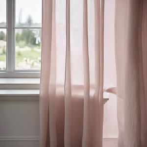 K&ouml;nnte beinhalten: Zwei durchsichtige rosa Vorh&auml;nge h&auml;ngen an einem Fenster und lassen Licht durch den Stoff scheinen.