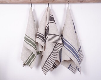 May include: Three striped linen tea towels hanging on a wooden rod. The towels are in shades of green, black, and blue.