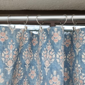 Peut inclure: Rideaux bleus avec un motif floral blanc et rose. Les rideaux sont suspendus à une tringle à rideaux argentée avec des anneaux argentés.