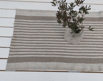 Puede incluir: Un camino de mesa de lino blanco con rayas marrones. El camino de mesa está sobre una superficie de madera blanca y un jarrón de vidrio con flores secas está encima del camino de mesa.