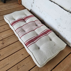 May include: A white linen cushion with red and white striped fabric and button tufting.