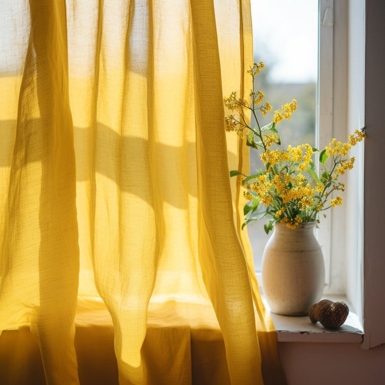 K&ouml;nnte beinhalten: Ein gelber, durchsichtiger Vorhang mit einer Vase voller gelber Blumen vor einem Fenster. Die Vase ist wei&szlig; und aus Keramik.