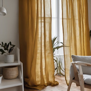 May include: A pair of sheer, mustard yellow linen curtains hang in a window. The curtains are gathered at the top and hang loosely, creating a relaxed and airy feel. The curtains are made of a lightweight fabric that allows light to filter through.