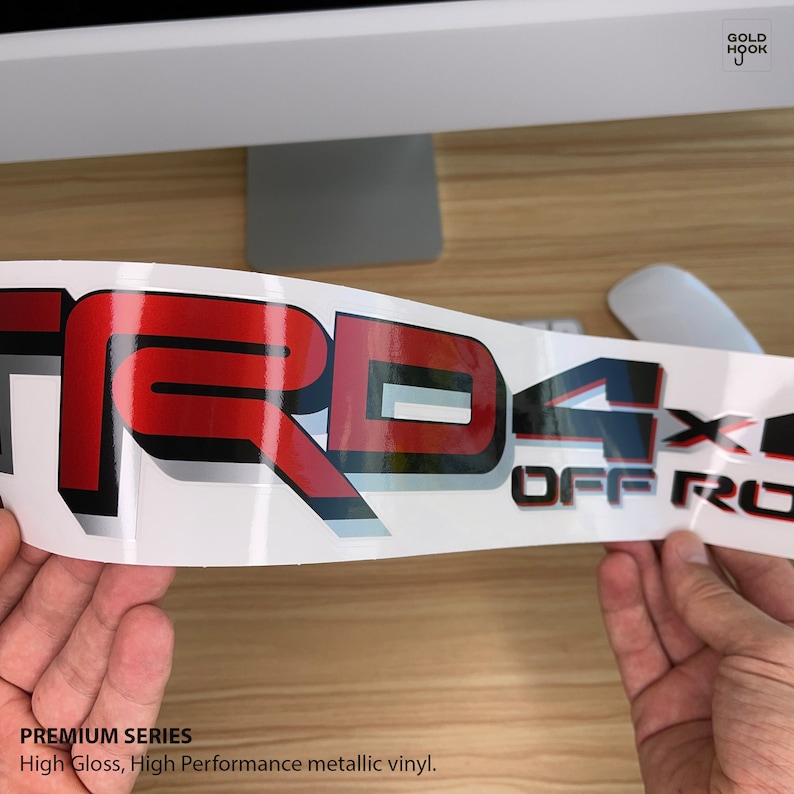May include: A red, black, and silver vinyl decal with the text "TRD 4X4 OFF ROAD" in a 3D style. The decal is on a white background and is designed for a vehicle.
