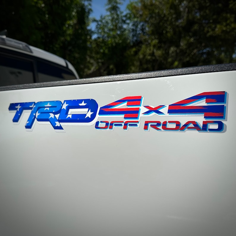 May include: A white truck tailgate with a red, white, and blue "TRD 4x4 OFF ROAD" decal. The decal features a stylized American flag design.