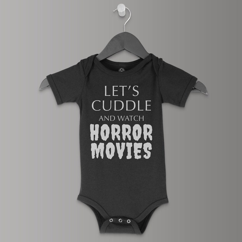 May include: A dark grey baby onesie with short sleeves and a white graphic that says "Let's cuddle and watch horror movies".