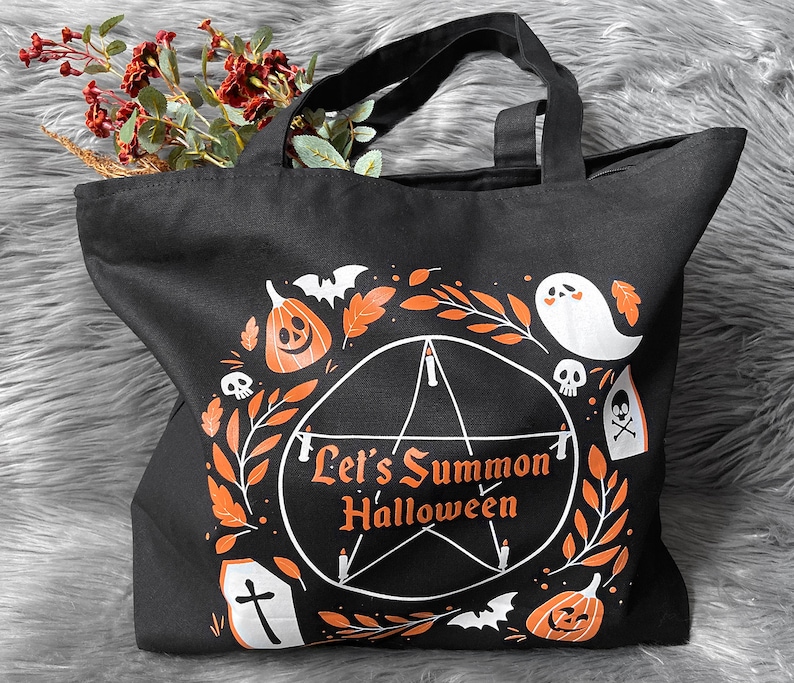 May include: Black canvas tote bag with a white pentagram design and the text "Let's Summon Halloween". The design also includes pumpkins, ghosts, bats, and other Halloween imagery.