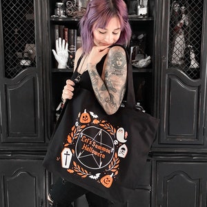 May include: Black tote bag with a white pentagram and the text "Let's Summon Halloween". The bag is decorated with orange pumpkins, bats, ghosts, and a skull and crossbones.