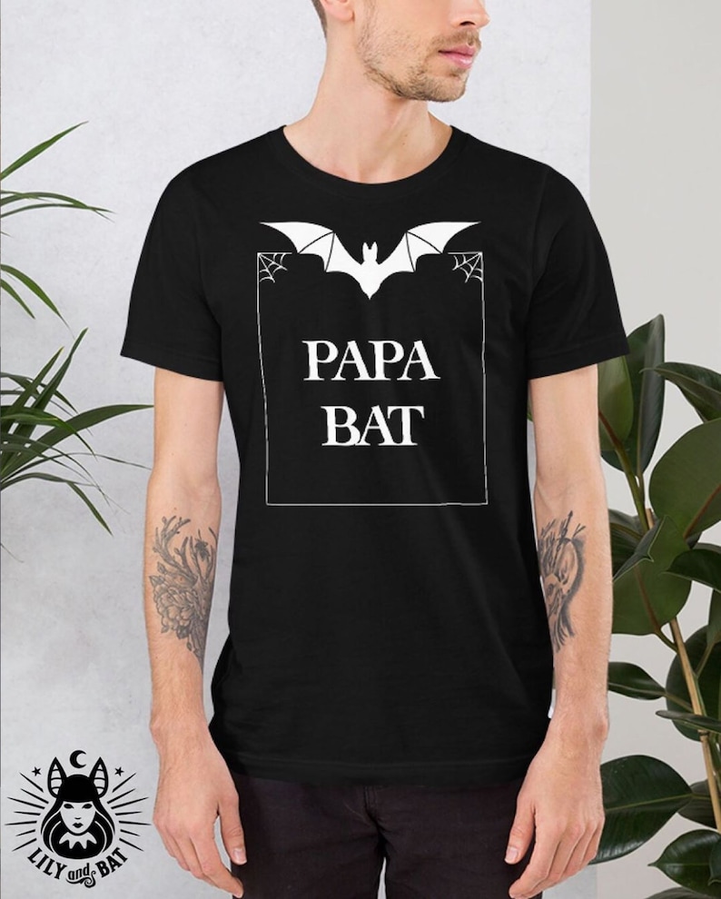 Pu&ograve; includere: Maglietta nera con una grafica di pipistrello bianca e il testo "Papa Bat" in una cornice bianca.