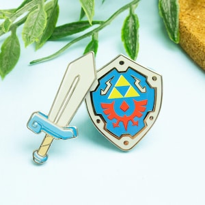 May include: A pin set featuring a sword and shield design. The sword has a white blade with a light blue hilt and gold handle. The shield is blue with a gold, red, and white emblem. The set is likely inspired by a video game.