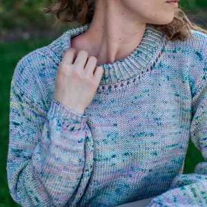 May include: A soft, multi-colored knit sweater with a round neckline and long sleeves. The sweater has a speckled pattern of pink, blue, green, and yellow.