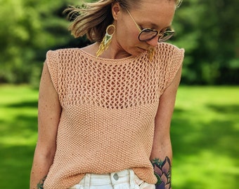 May include: A peach-colored sleeveless knit top featuring a textured garter stitch lower section and an open, airy mesh stitch pattern across the upper chest and shoulders, paired with white denim shorts with a subtle peach tie-dye wash.