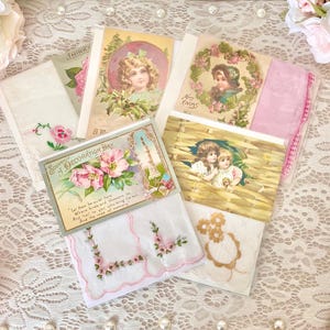 May include: Assortment of vintage handkerchiefs with floral and angel designs. The handkerchiefs are white with pink and blue embroidery. The handkerchiefs are displayed on a white lace tablecloth with pink roses.