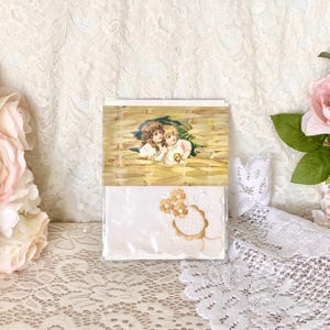 May include: A white handkerchief with gold embroidery of two flowers in a circle. The handkerchief is packaged in a clear plastic sleeve with a vintage postcard featuring two children in a field of wheat.