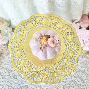 May include: A pink glittery pumpkin with a floral embellishment sits on a gold paper doily.