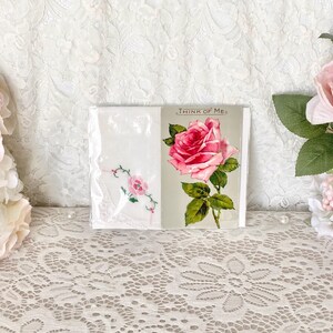 May include: Two white handkerchiefs with pink rose embroidery. One handkerchief has the text "Think of Me" printed on it. The handkerchiefs are displayed on a white lace tablecloth.