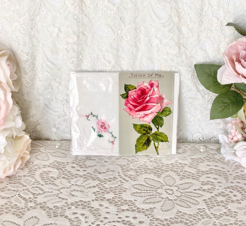 May include: Two white handkerchiefs with pink rose embroidery. One handkerchief has the text "Think of Me" printed on it. The handkerchiefs are displayed on a white lace tablecloth.