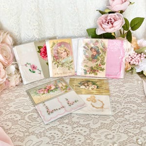 May include: A collection of vintage handkerchiefs and postcards with floral and holiday themes. The handkerchiefs are white with pink embroidery and the postcards feature images of children and flowers.