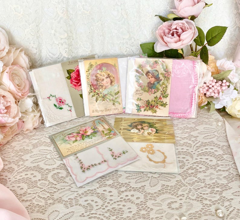 May include: A collection of vintage handkerchiefs and postcards with floral and holiday themes. The handkerchiefs are white with pink embroidery and the postcards feature images of children and flowers.