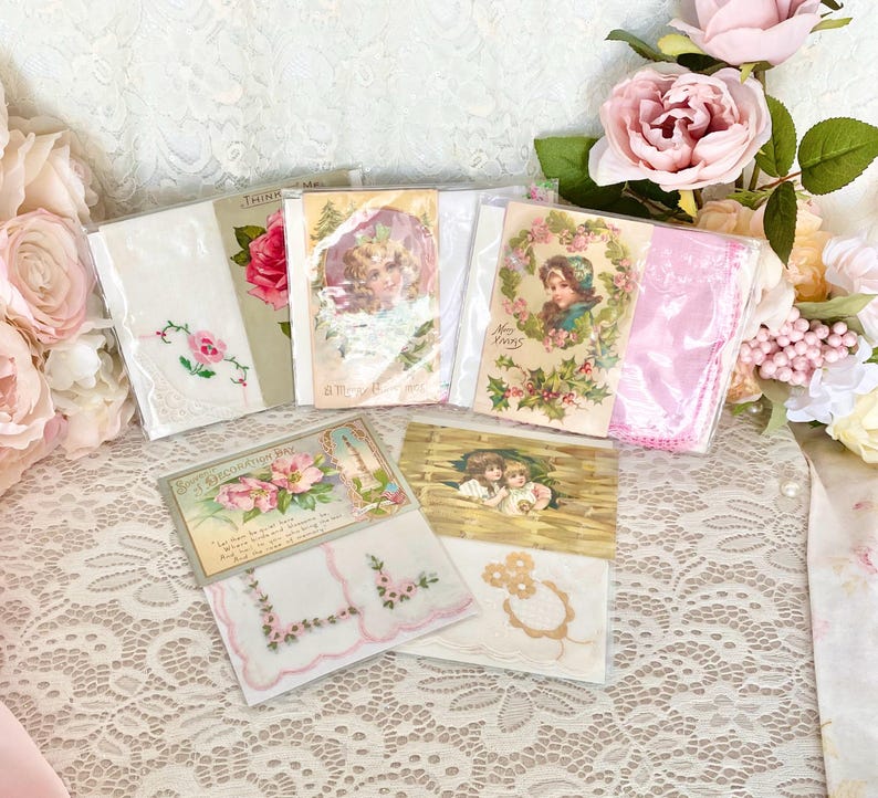 May include: A collection of vintage handkerchiefs and postcards with floral and lace designs. The handkerchiefs are white with pink embroidery and the postcards feature images of children and flowers.
