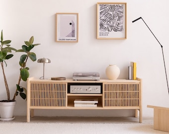 May include: A light wood cabinet with slatted doors and two shelves. The cabinet has a record player on top and a stereo receiver on the lower shelf. There are two framed prints on the wall behind the cabinet, one with the text "GALERIE TEMPORAIRE" and the other with the text "MALENE BIRGER".