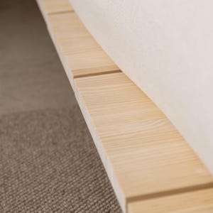 Puede incluir: Primer plano de una estructura de cama de madera clara con acabado natural. La estructura est&aacute; construida con tablones rectangulares, con vetas de madera visibles. Se ve una secci&oacute;n de un colch&oacute;n color crema.