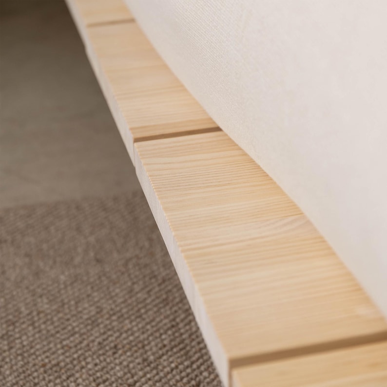 Puede incluir: Primer plano de una estructura de cama de madera clara con acabado natural. La estructura est&aacute; construida con tablones rectangulares, con vetas de madera visibles. Se ve una secci&oacute;n de un colch&oacute;n color crema.