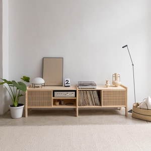 May include: A light wood entertainment center with two doors, two shelves, and a record player on top. The center has a slatted design on the doors and is sitting on a light beige rug.
