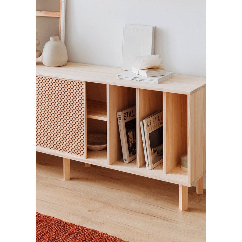 May include: A light wood cabinet with a woven wood door and shelves. The cabinet has four compartments and is filled with books and magazines, including "Cereal" and "Still" magazines.