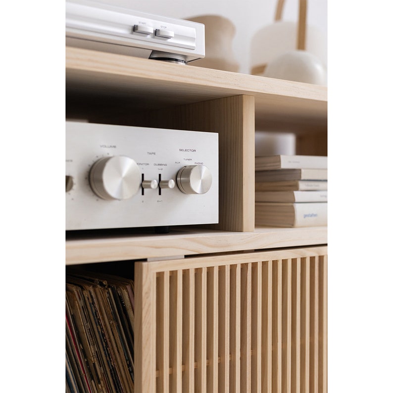 May include: A light wood entertainment center with a record player, amplifier, and books on the shelves. The bottom shelf has a slatted door that hides a record collection.