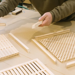 Pu&ograve; includere: Una persona sta lavorando a un progetto di artigianato in legno. Sta tenendo un pezzo di legno e ci sono diversi altri pezzi di legno sul tavolo. Il legno &egrave; marrone chiaro e ha una finitura naturale.