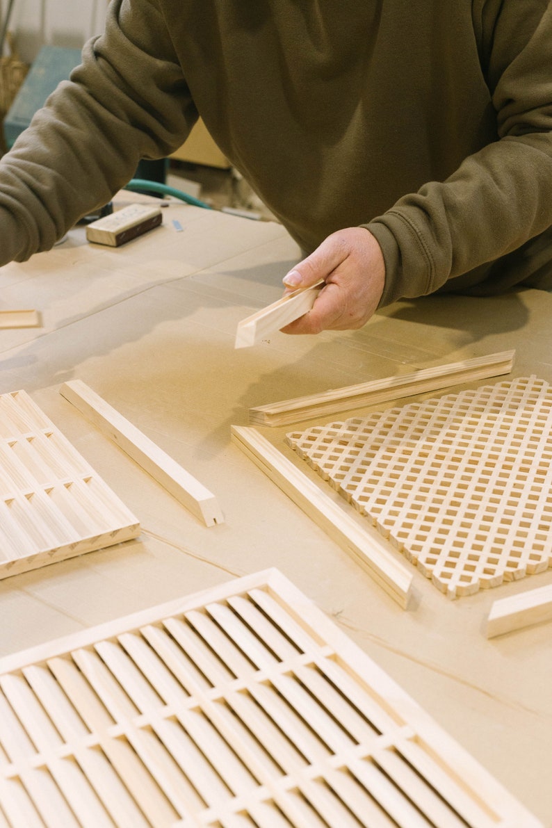 Pu&ograve; includere: Una persona sta lavorando a un progetto di artigianato in legno. Sta tenendo un pezzo di legno e ci sono diversi altri pezzi di legno sul tavolo. Il legno &egrave; marrone chiaro e ha una finitura naturale.