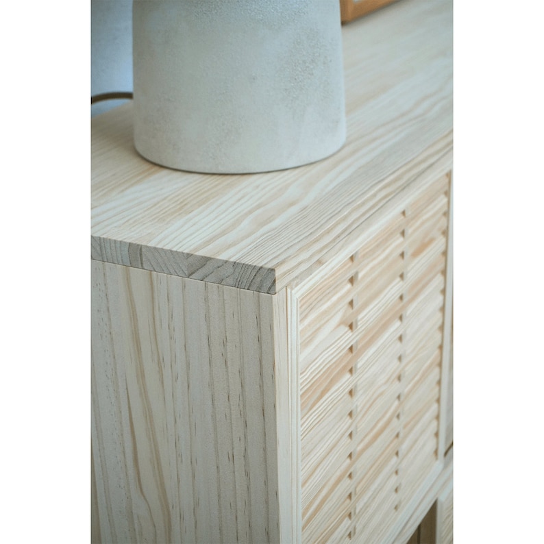 May include: A light wood cabinet with a slatted door and a smooth top. The cabinet is made of natural wood with a light finish.