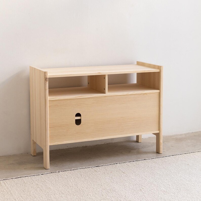 May include: A light wood cabinet with a drawer and two shelves. The cabinet has a simple, modern design and is made of natural wood.
